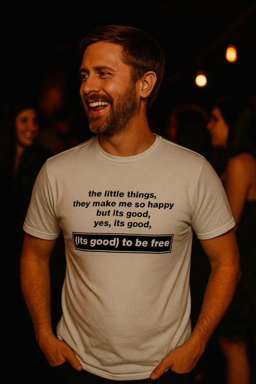 Man wearing a white t-shirt with text, standing in a dimly lit setting.